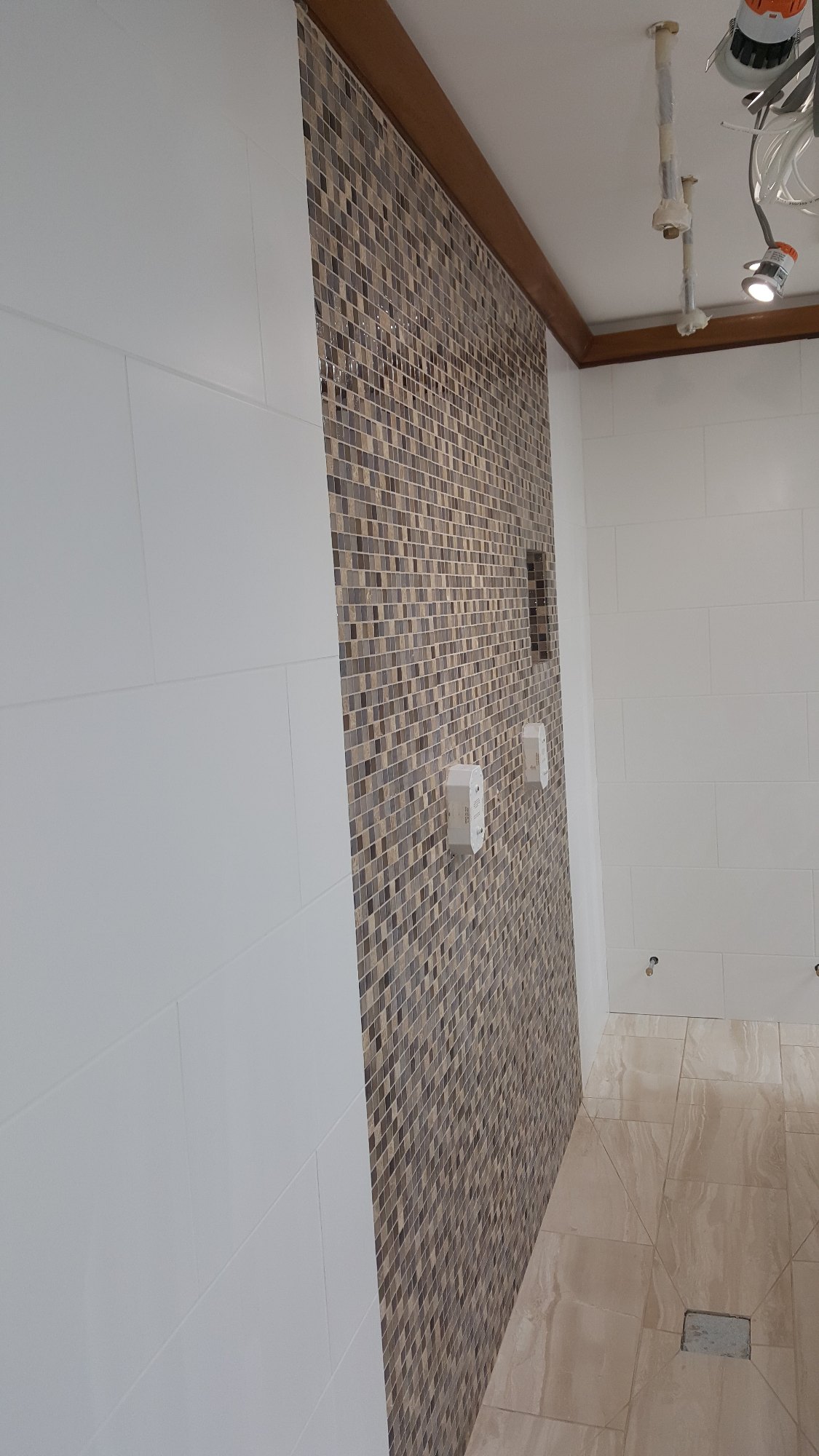 The mosaic feature wall and stone-effect floor tiles were precisely fitted around the shower fittings and drainage point.