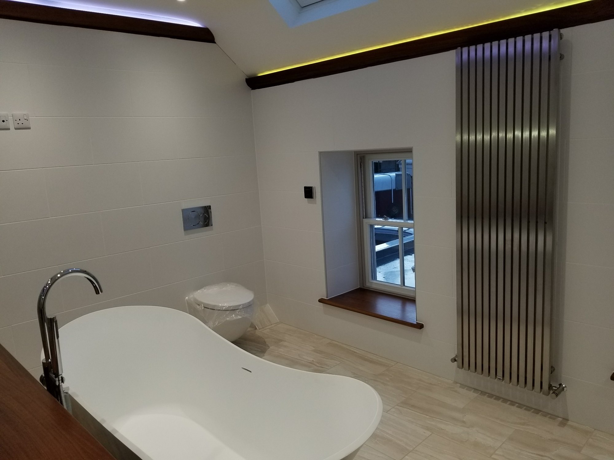 The completed bathing area combines a freestanding bath, floor-mounted tap, wall-hung toilet and contemporary vertical radiator.