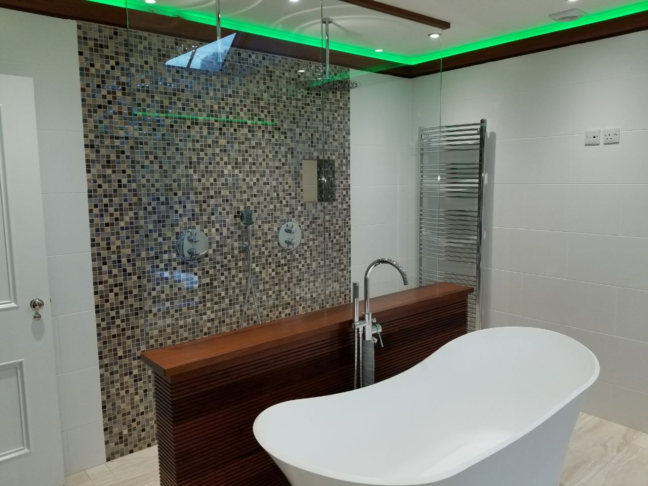 The finished bathroom brings together the walk-in shower, freestanding bath, bespoke woodwork, mosaic detailing and atmospheric lighting in one luxurious space.