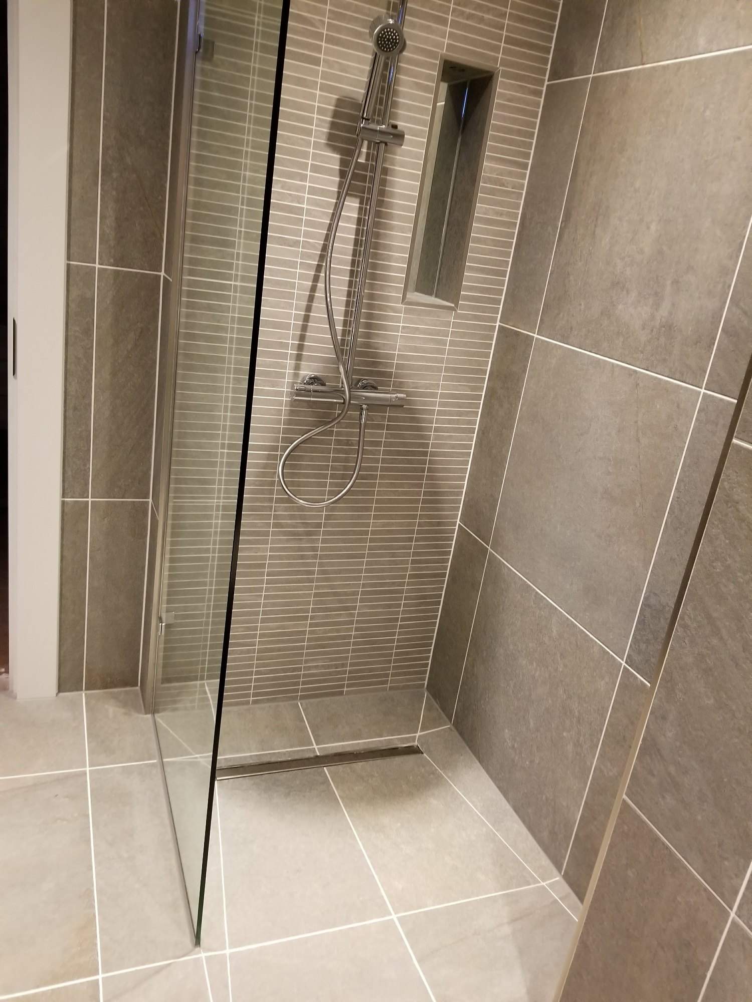 The narrow-format tiles create a subtle focal point behind the rainfall and handheld shower system.