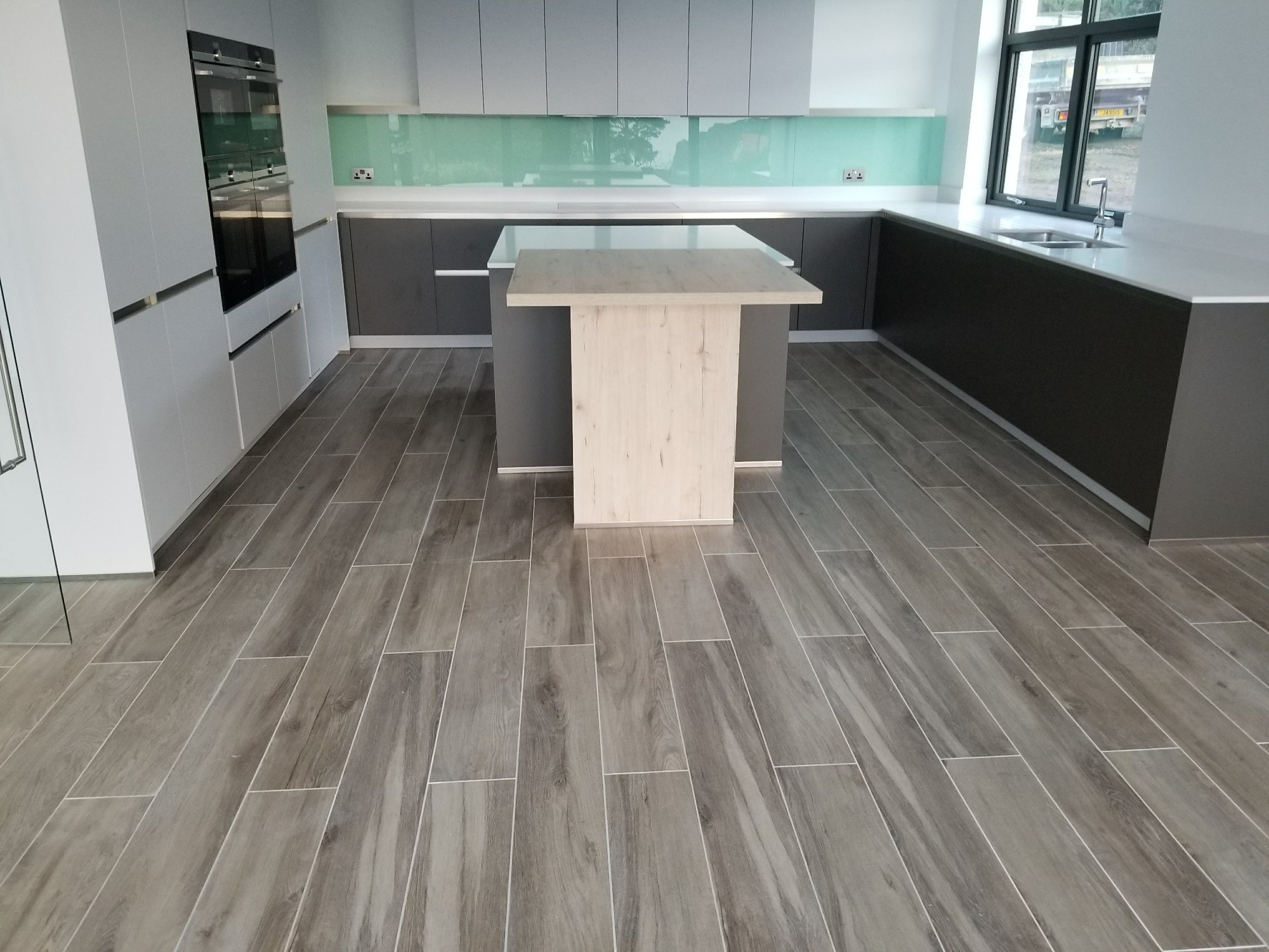 Wood-effect porcelain tiles complement the modern kitchen units while providing a practical and easy-to-clean surface.