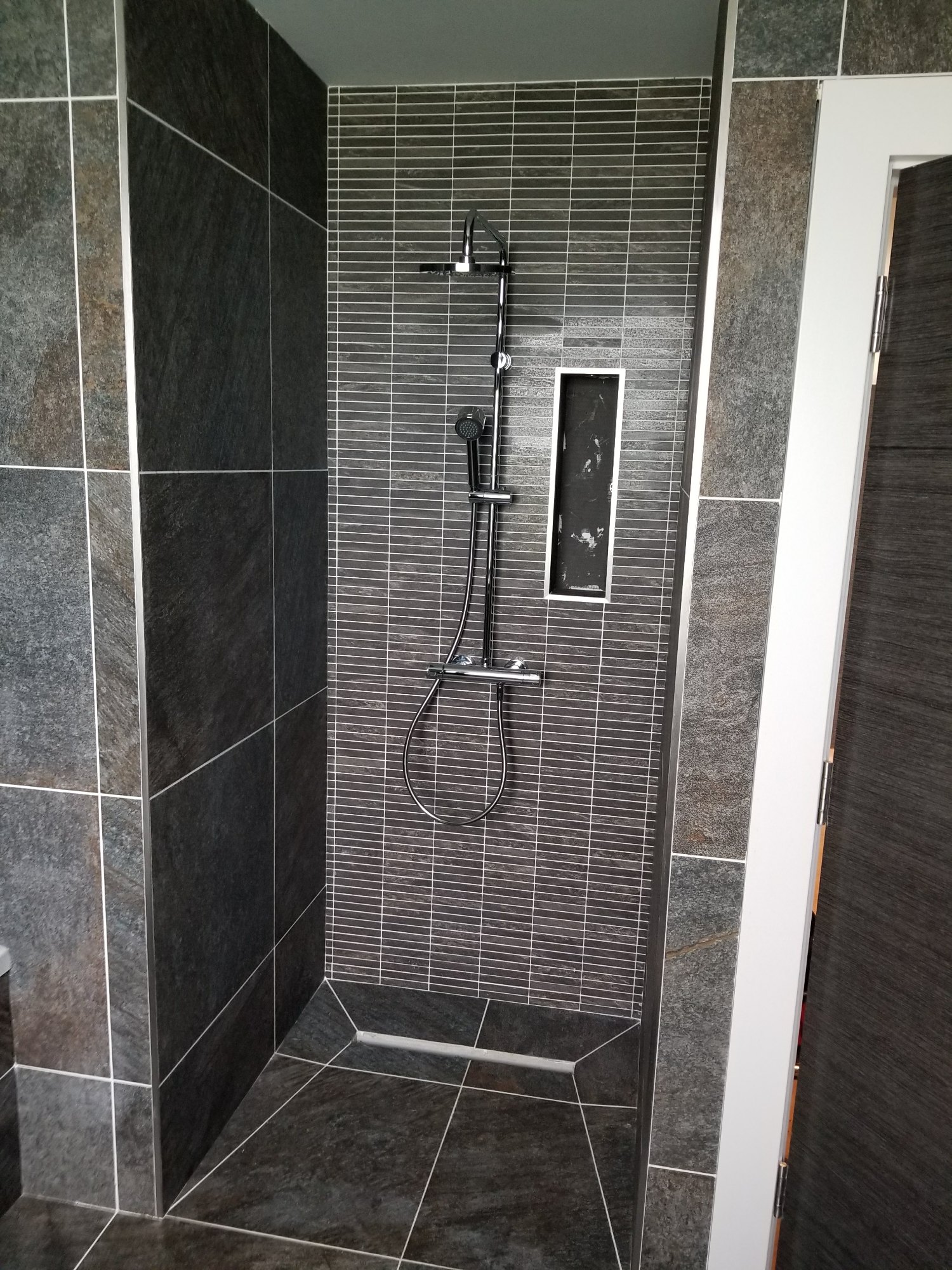 La douche à l’italienne terminée comprend une douche pluie, une douchette et une niche de rangement encastrée pratique.