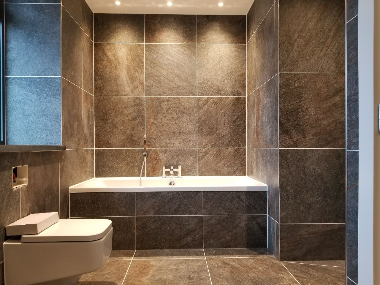 A front view of the completed bathroom showing the tiled bath, wall-hung toilet and carefully arranged spotlights.