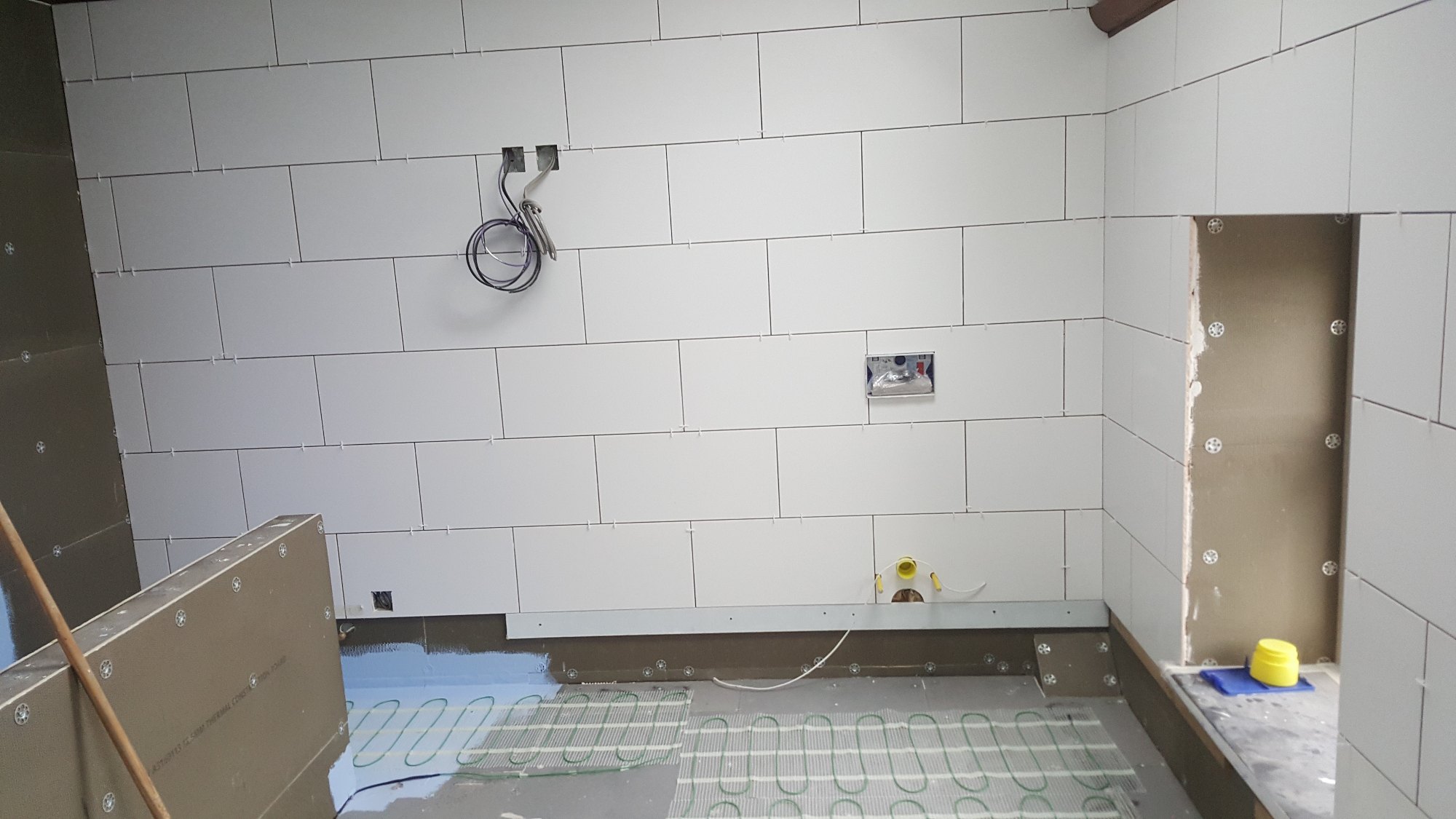 Le système de chauffage électrique a été installé pendant que se poursuivait la pose des grands carreaux blancs sur les murs.