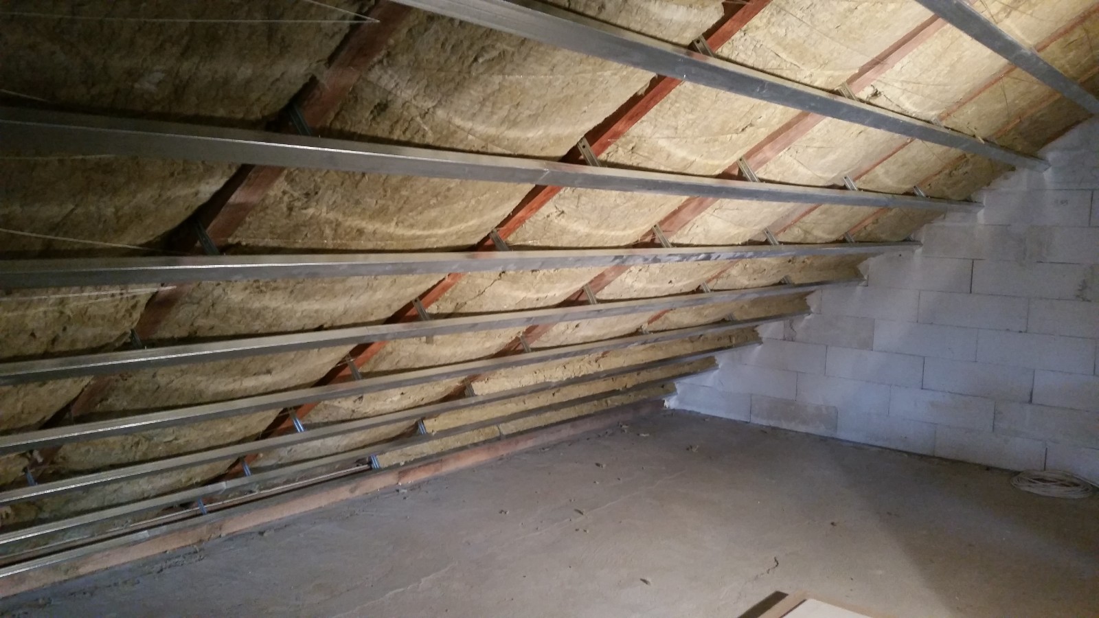 Attic roof insulation with exposed timber rafters and metal framing for plasterboard.