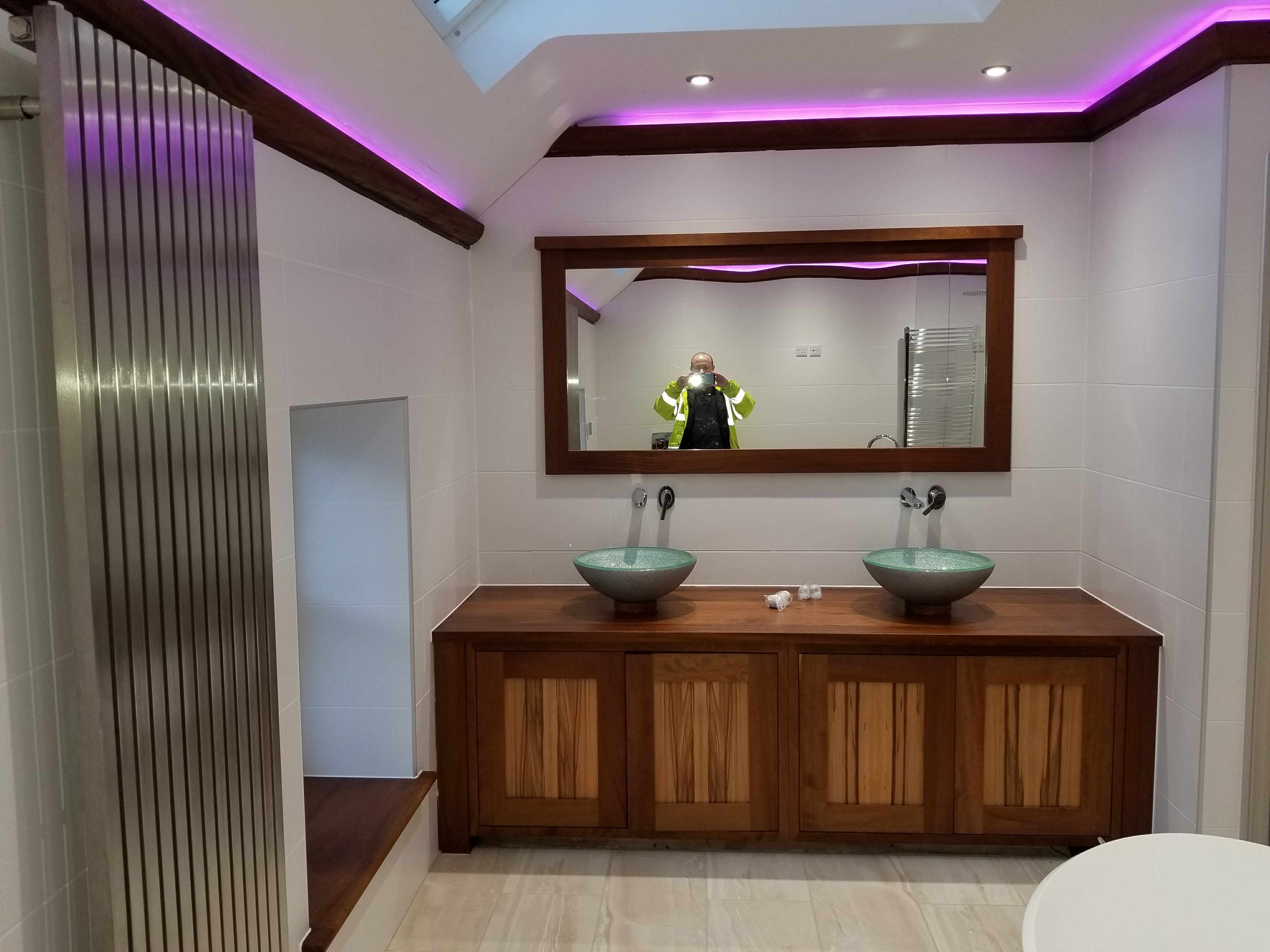 Bathroom with a wooden double vanity, two bowl basins, a framed mirror and purple ceiling lighting.