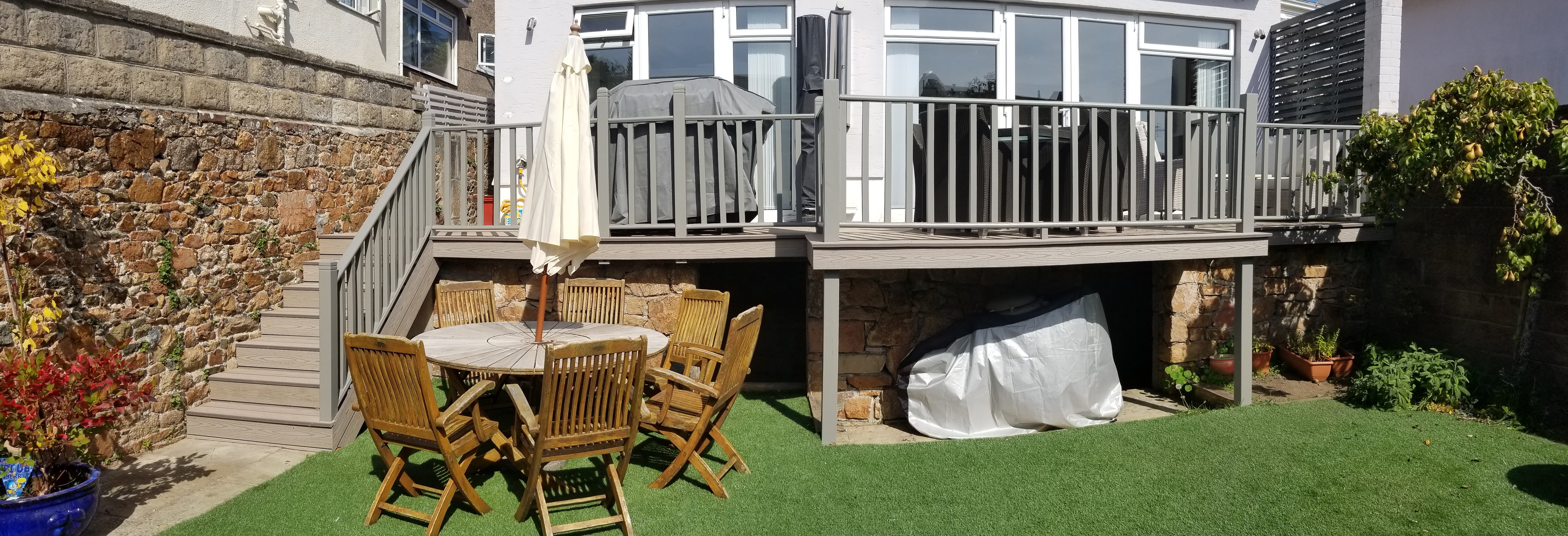 Raised grey garden deck with matching balustrade and stairs beside the house.